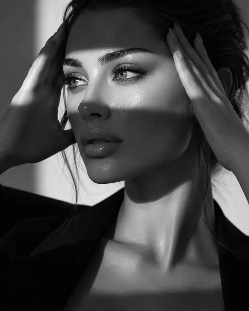 A black and white close portrait of a model in hard window light with both hands raised to the sides of her head, and photographs from a studio shoot